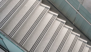 gray terrazzo staircase with three black abrasive strips and a blue glass railing
