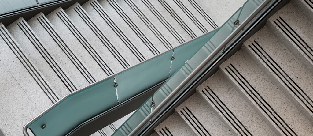 gray terrazzo staircase with three black abrasive strips and a blue glass railing